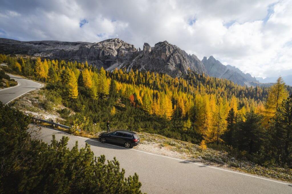 Man on side of road taking photo of fall colors