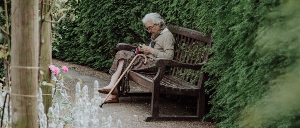 Grandma with cane sitting at bench looking at her smart phone.